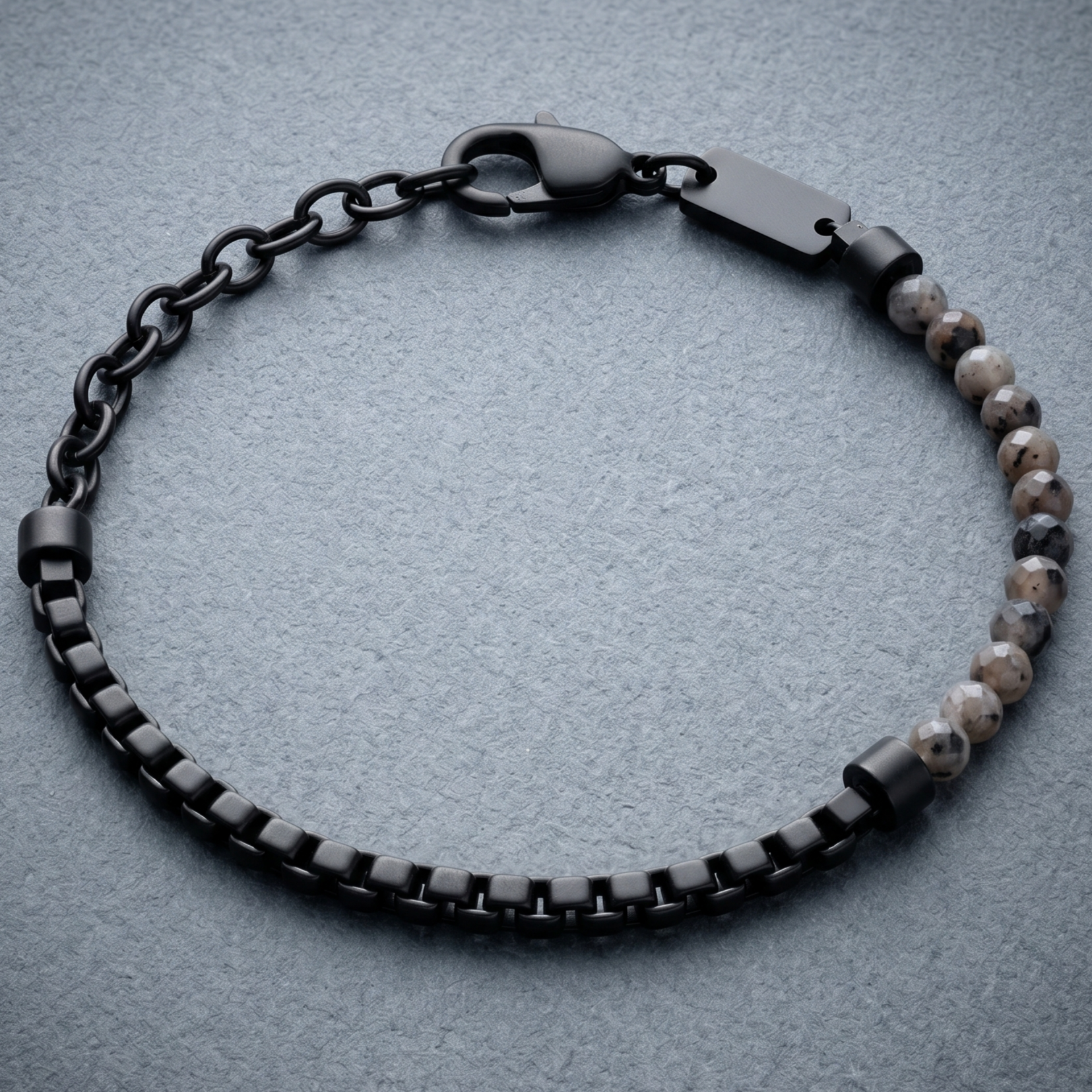 Black men's bracelet with matte stainless steel chain links, faceted grey stone beads and lobster clasp on stone surface