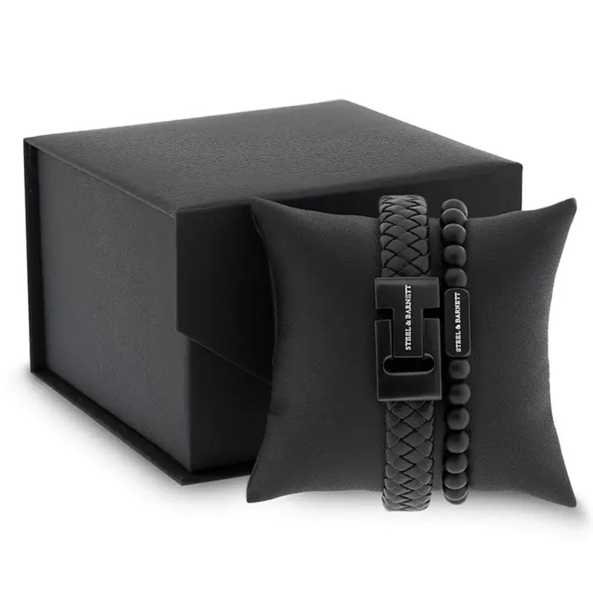 Black braided leather men’s bracelet with matte black stainless steel clasp and matching beaded bracelet displayed on a black cushion beside a gift box