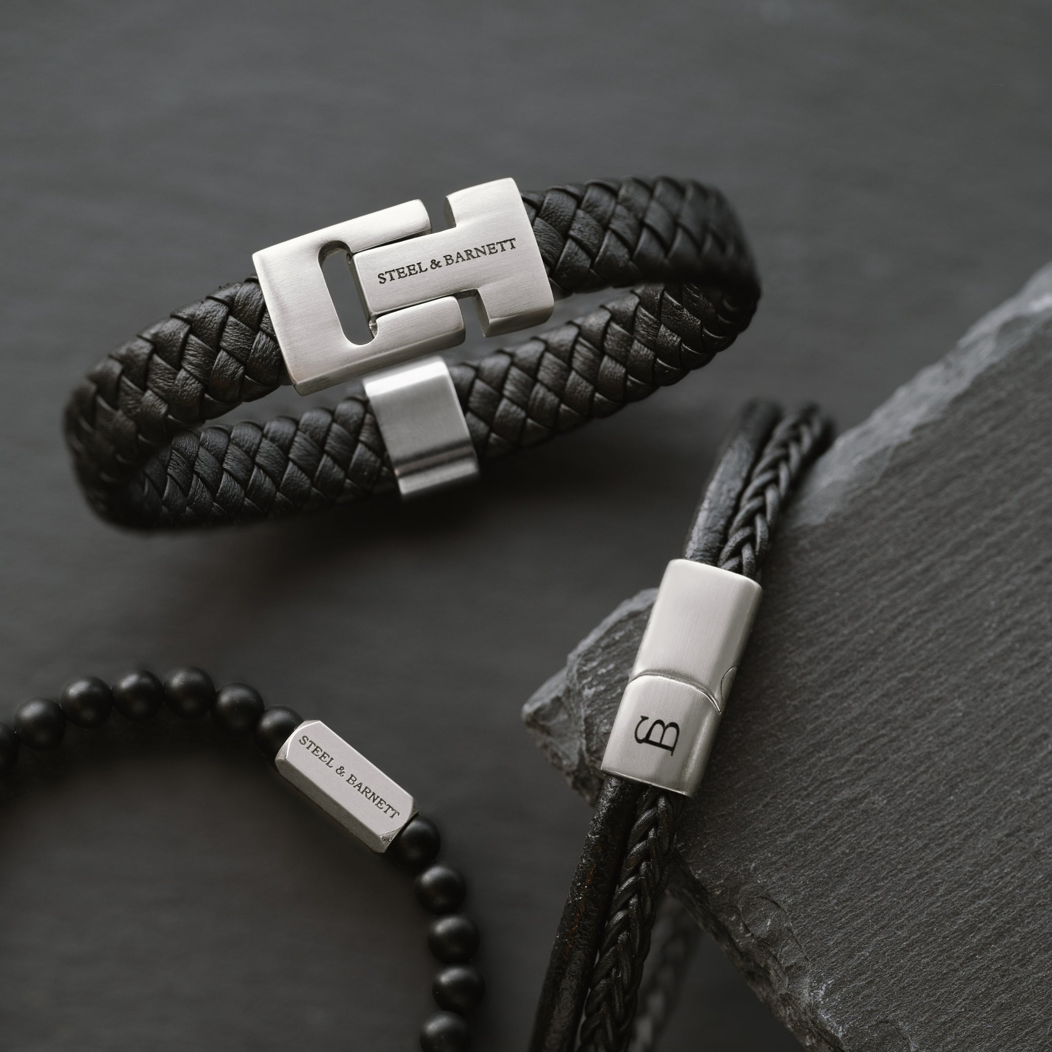 close-up of stacked men’s black leather bracelets with braided leather and matte beads highlighting brushed stainless steel clasp details