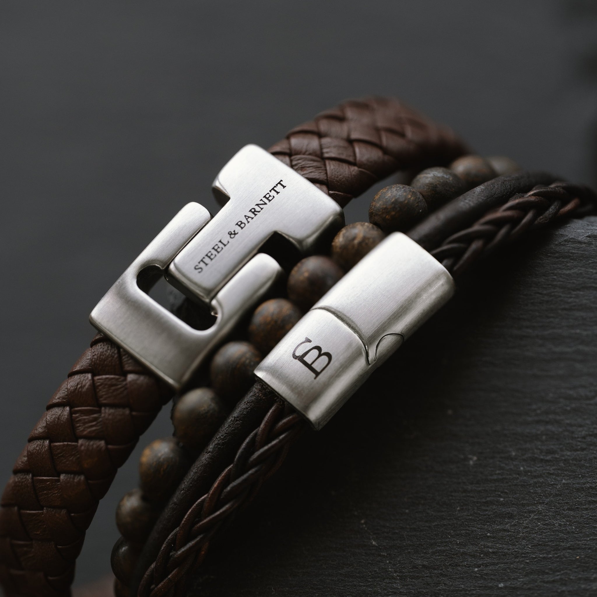 close-up of stacked men’s brown leather bracelets with braided leather and natural stone beads highlighting brushed stainless steel clasp details