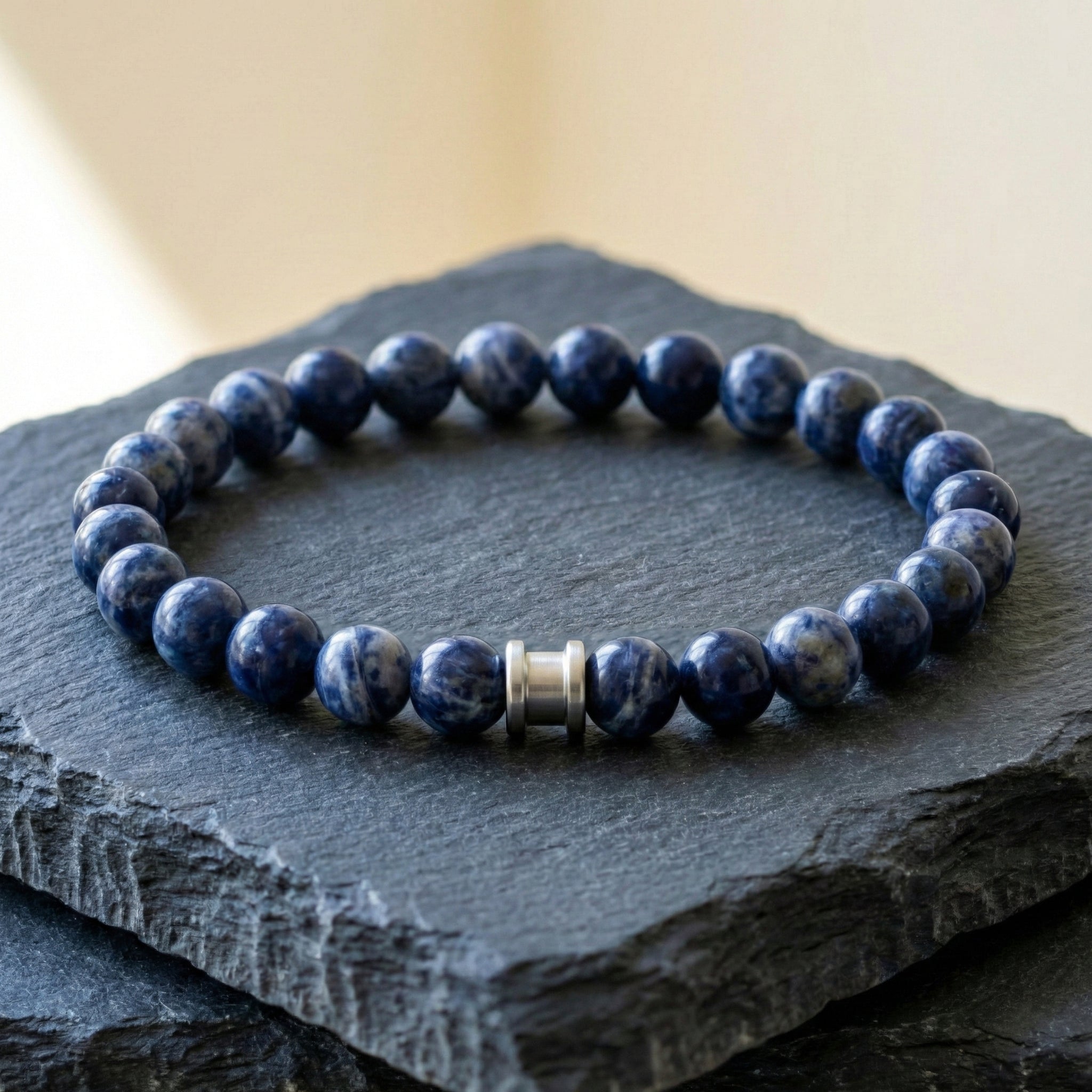 Blue natural stone men’s bracelet with round polished beads and stainless steel detail on a dark slate surface