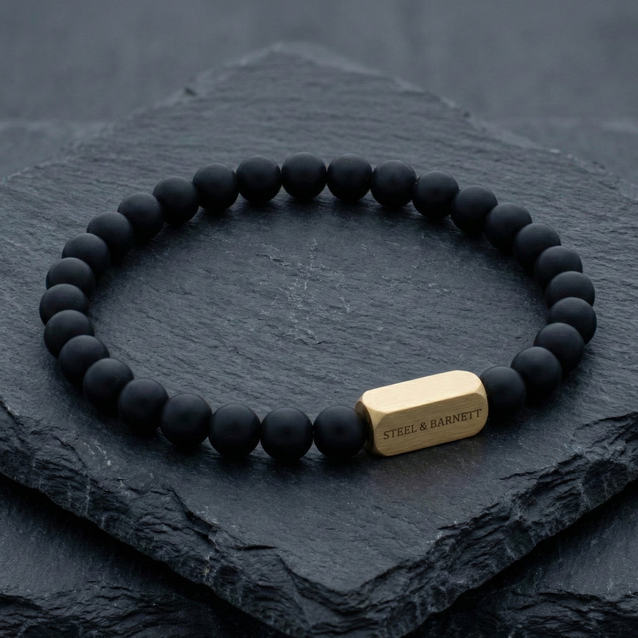 Black beads and plated 18K gold clasp on dark stone surface