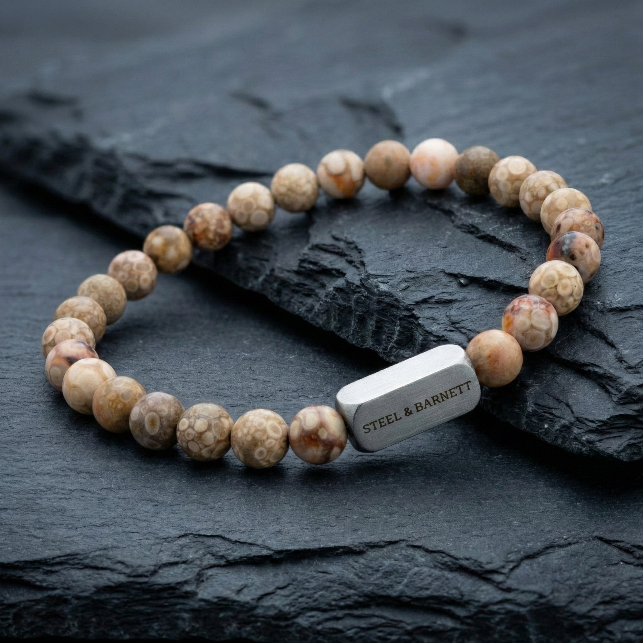 Maifanite men’s bracelet with beige patterned beads and brushed stainless steel bar on dark stone surface