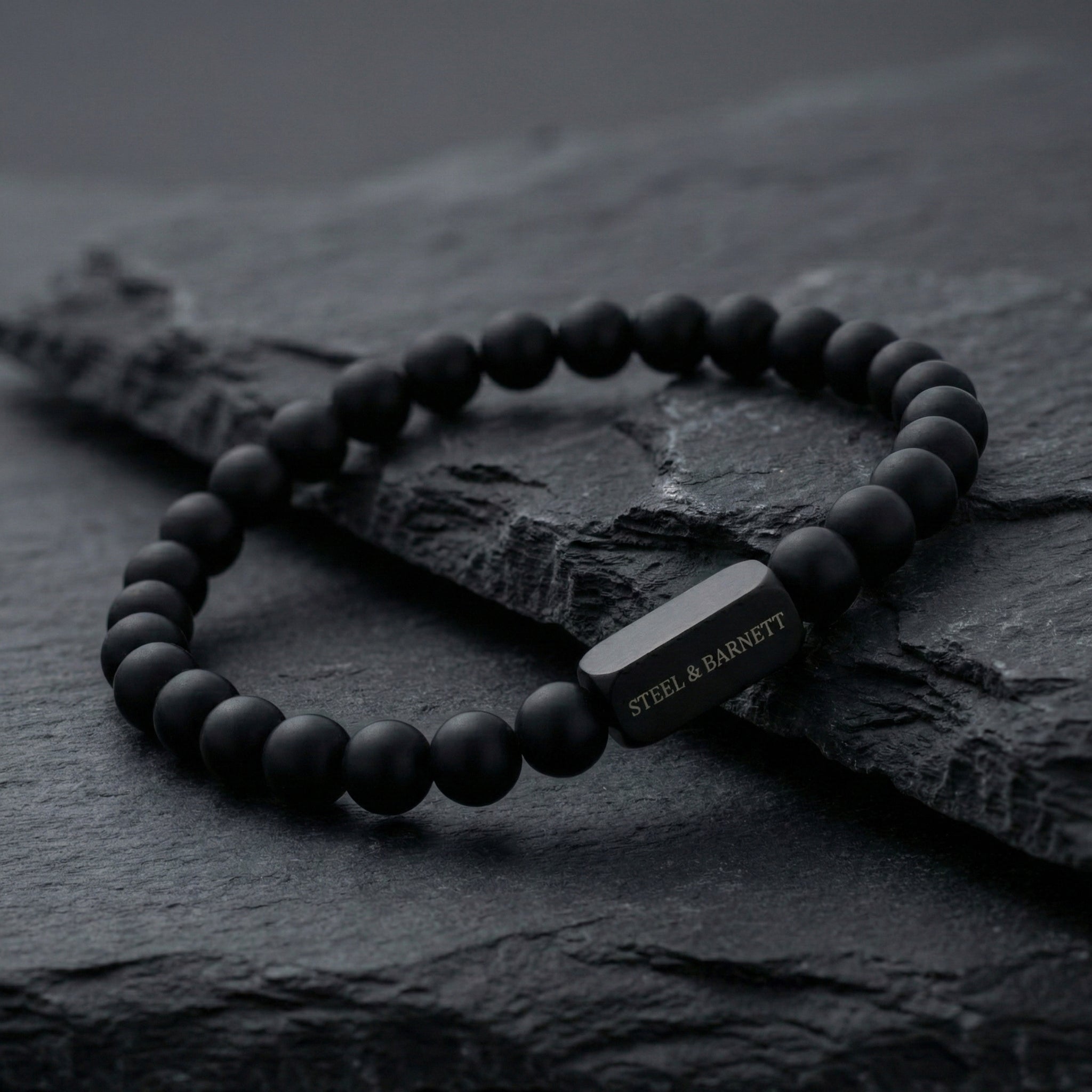 Black onyx men’s bracelet with matte stone beads and black stainless steel bar worn on wrist with hand in pocket