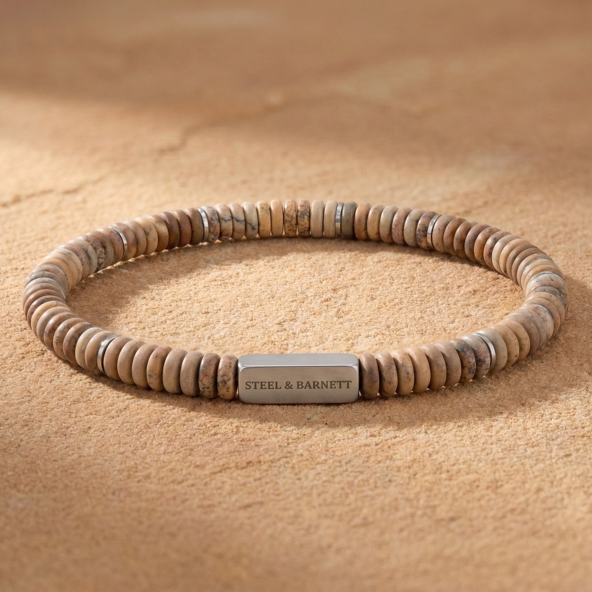 Picture jasper natural stone men's beaded bracelet with matte disc beads and brushed stainless steel accent plate on a sandy surface close up detail