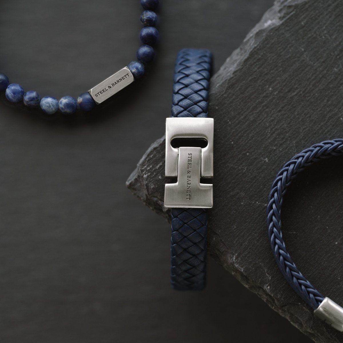 Blue braided leather men’s bracelet with brushed stainless steel clasp detail shown on a dark stone surface