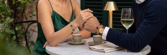 Black and green clover bracelets with gold tone details worn by a couple holding hands at an outdoor café