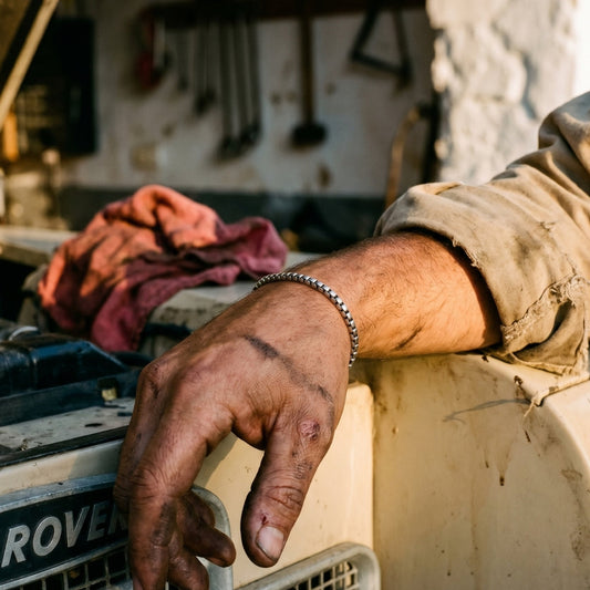 Silver stainless steel men's chain bracelet worn on wrist beside a vintage vehicle in a workshop setting