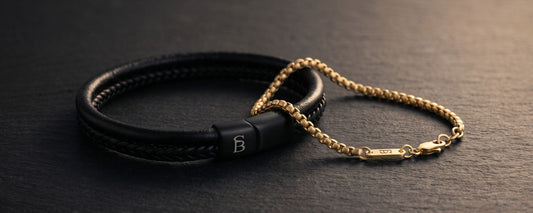 Black braided leather men's bracelet with a black clasp and a plated 18K gold chain bracelet displayed on a dark surface