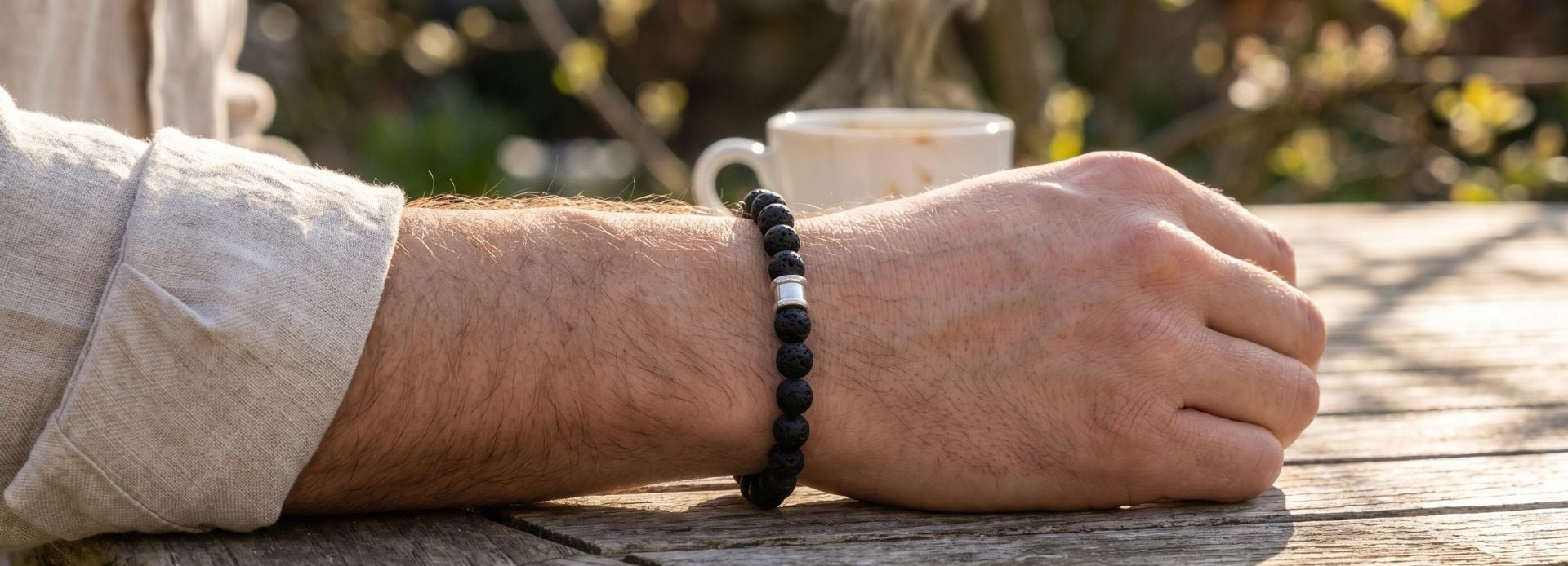 Black beaded men's bracelet with matte stone beads and a single stainless steel accent bead worn on wrist outdoors on a wooden table