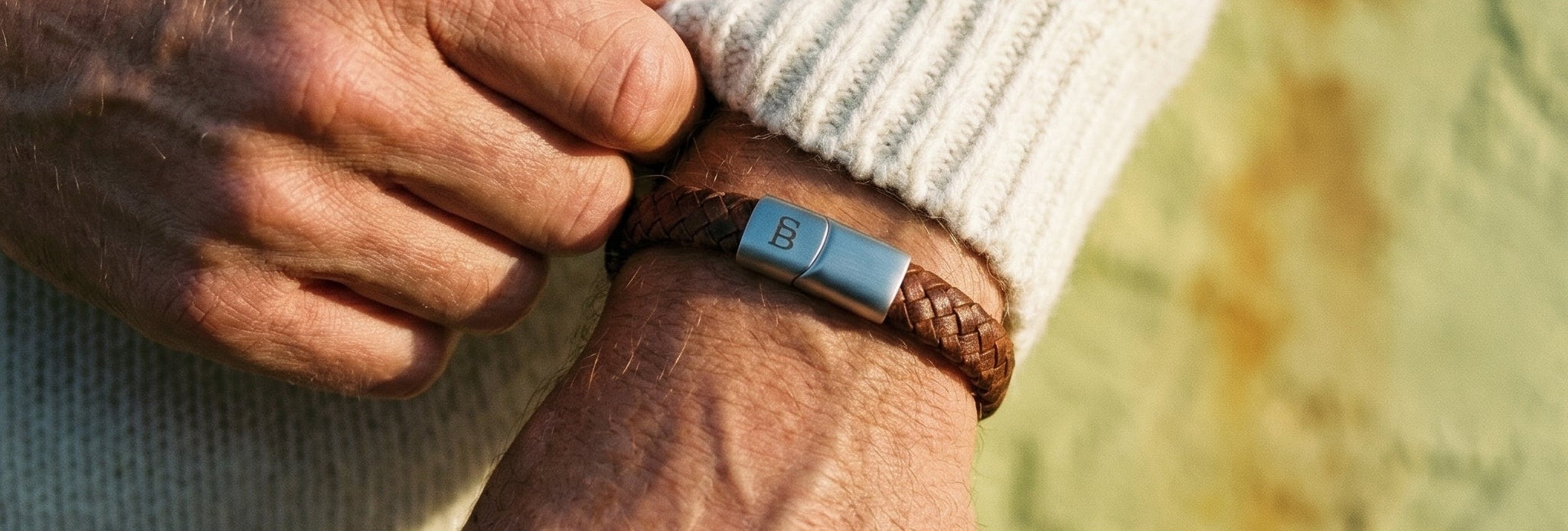 Close-up of a person adjusting a brown leather bracelet on their wrist with a blurred natural background.