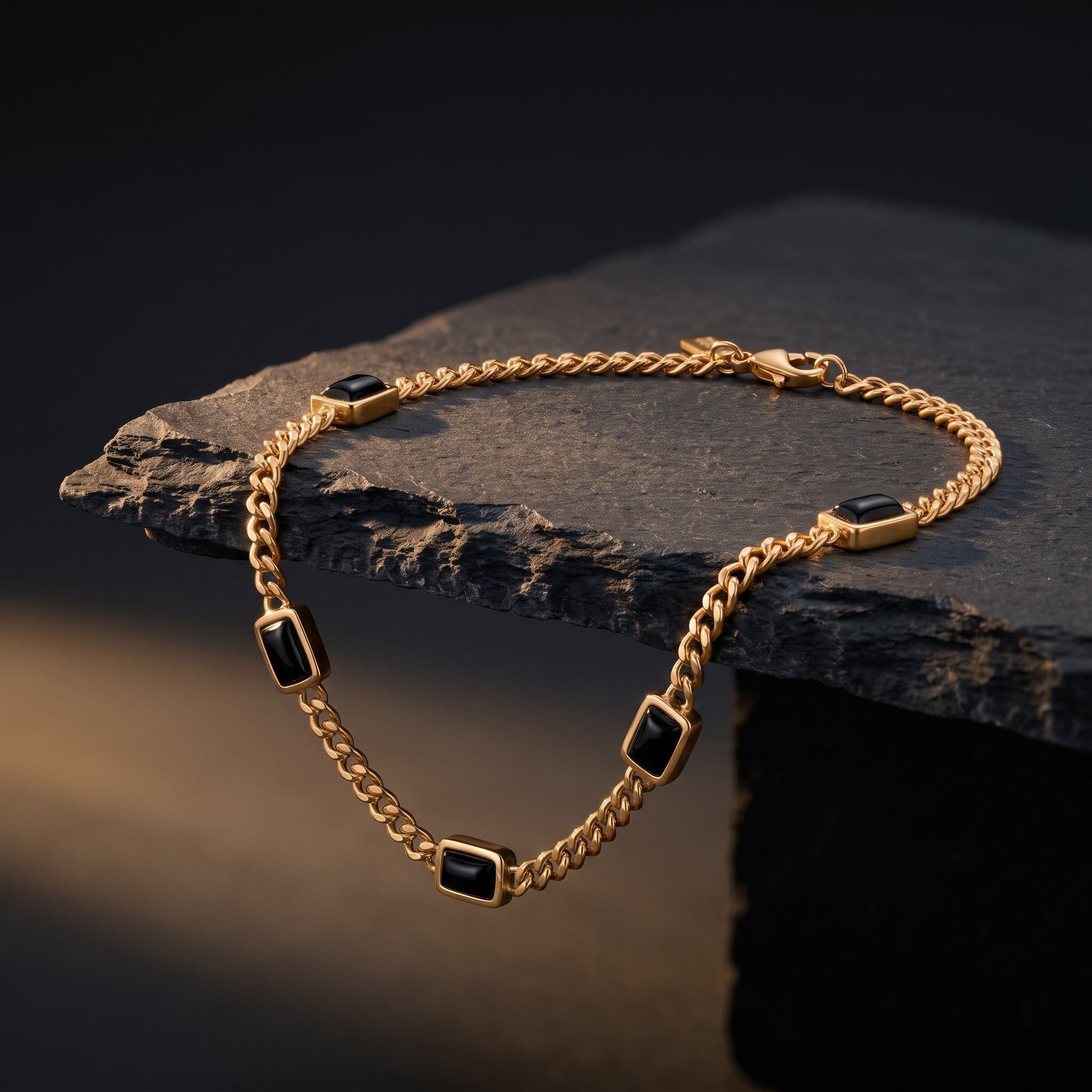 Gold chain men's bracelet with black rectangular stone accents and a plated 18K gold clasp on a dark stone surface