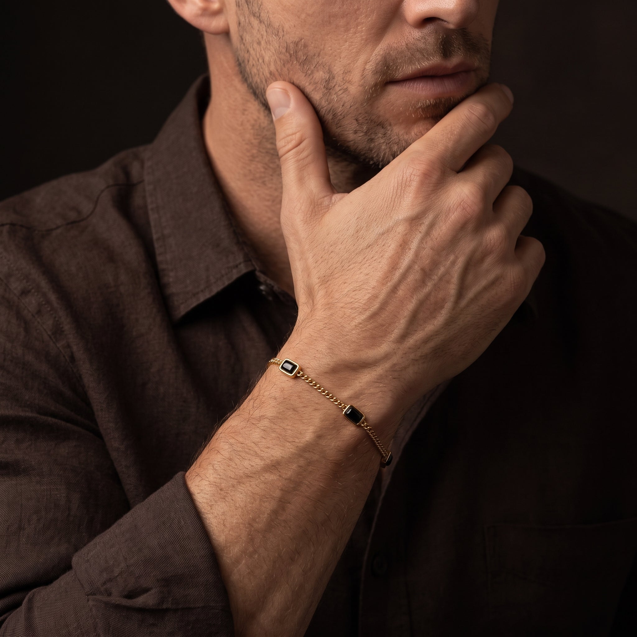 Gold chain men's bracelet with black rectangular stone accents shown on the wrist in a close up lifestyle view