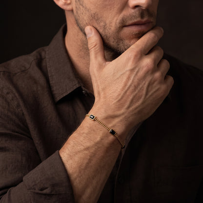 Gold chain men's bracelet with black rectangular stone accents shown on the wrist in a close up lifestyle view