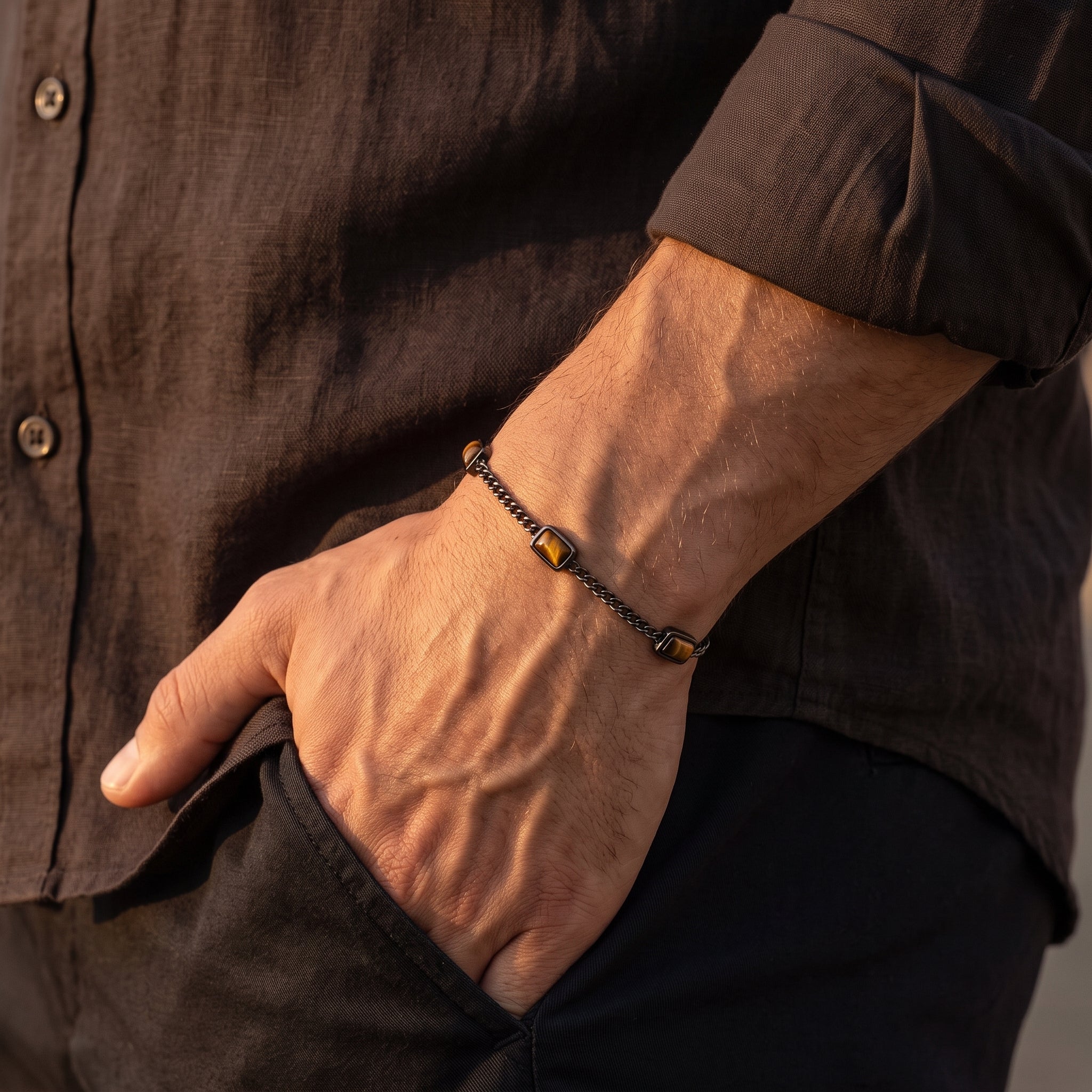 Dark metal chain men's bracelet with rectangular brown stone accents worn on the wrist with a dark brown shirt