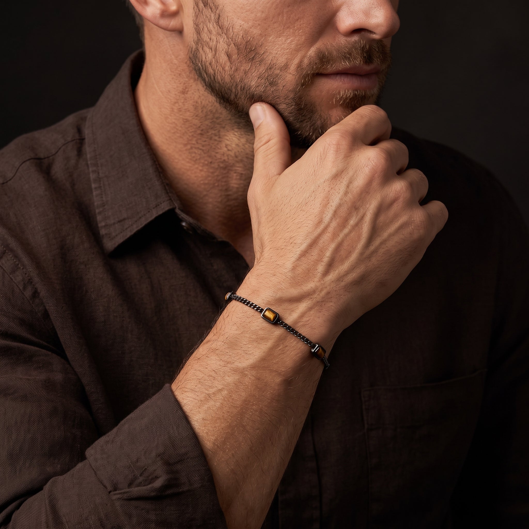 Dark metal chain men's bracelet with rectangular brown stone accents worn on the wrist in a close up lifestyle view