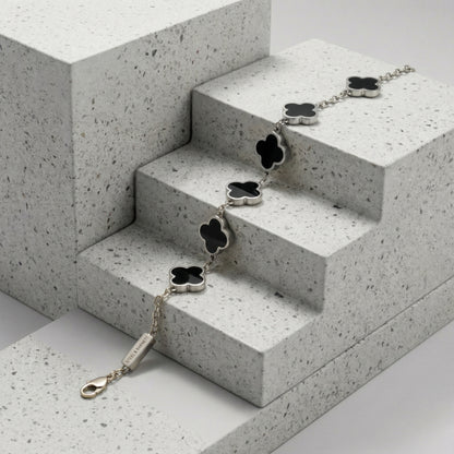 Silver toned men’s bracelet with black clover shaped inlays in stainless steel chain displayed on textured stone surface