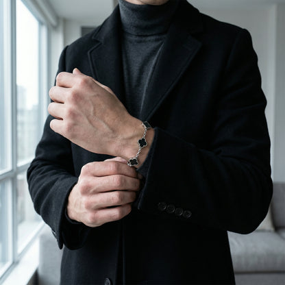 Silver toned men’s bracelet with black clover shaped inlays in stainless steel chain worn on wrist with black coat