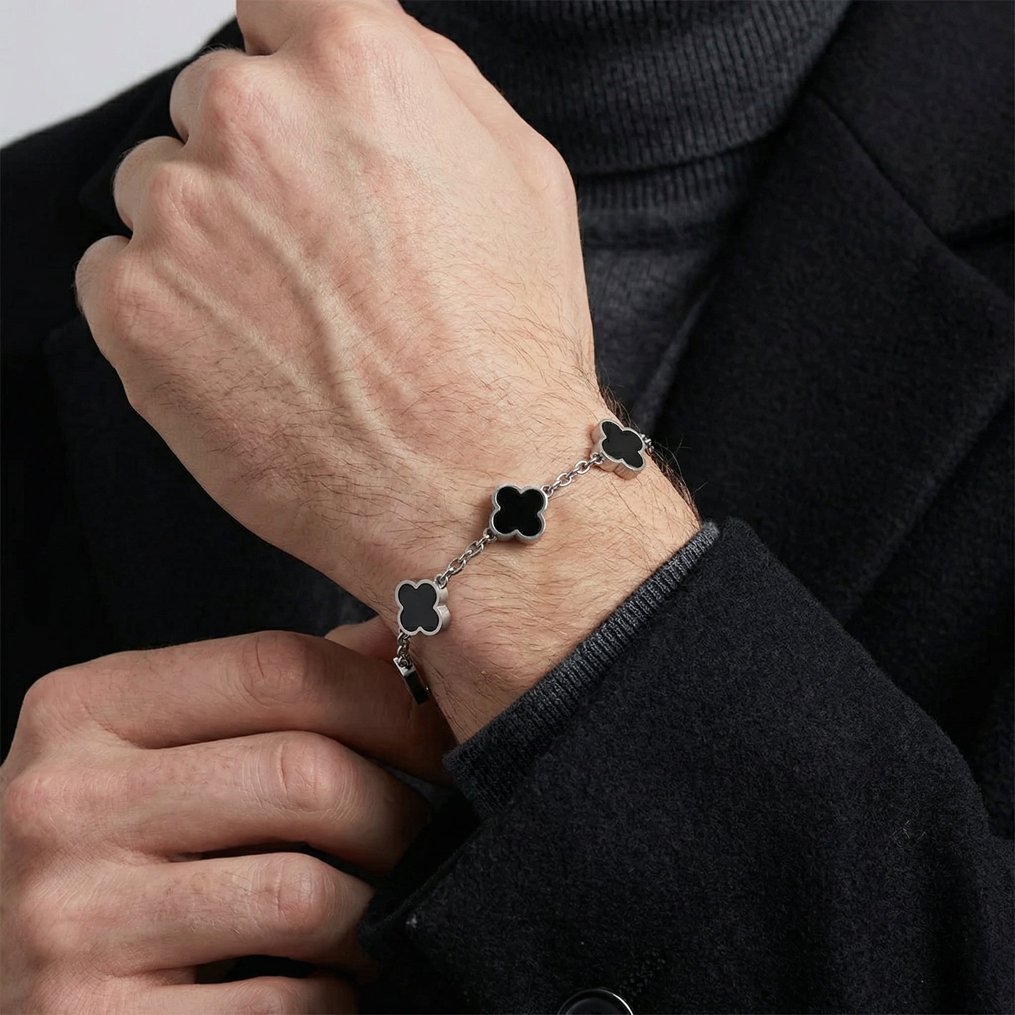 Silver toned men’s bracelet with black clover shaped inlays in stainless steel chain shown as close up on wrist