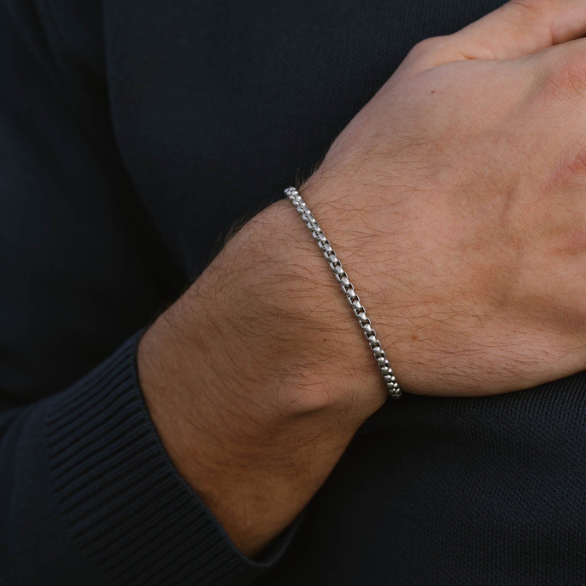 Silver stainless steel men's bracelet with box chain links and lobster clasp with small engraved tag detail on a white background