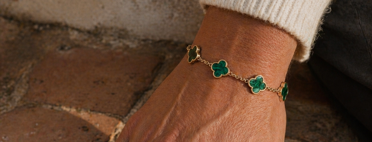 Green clover bracelet with plated 18K gold chain links worn on a wrist against a stone surface background