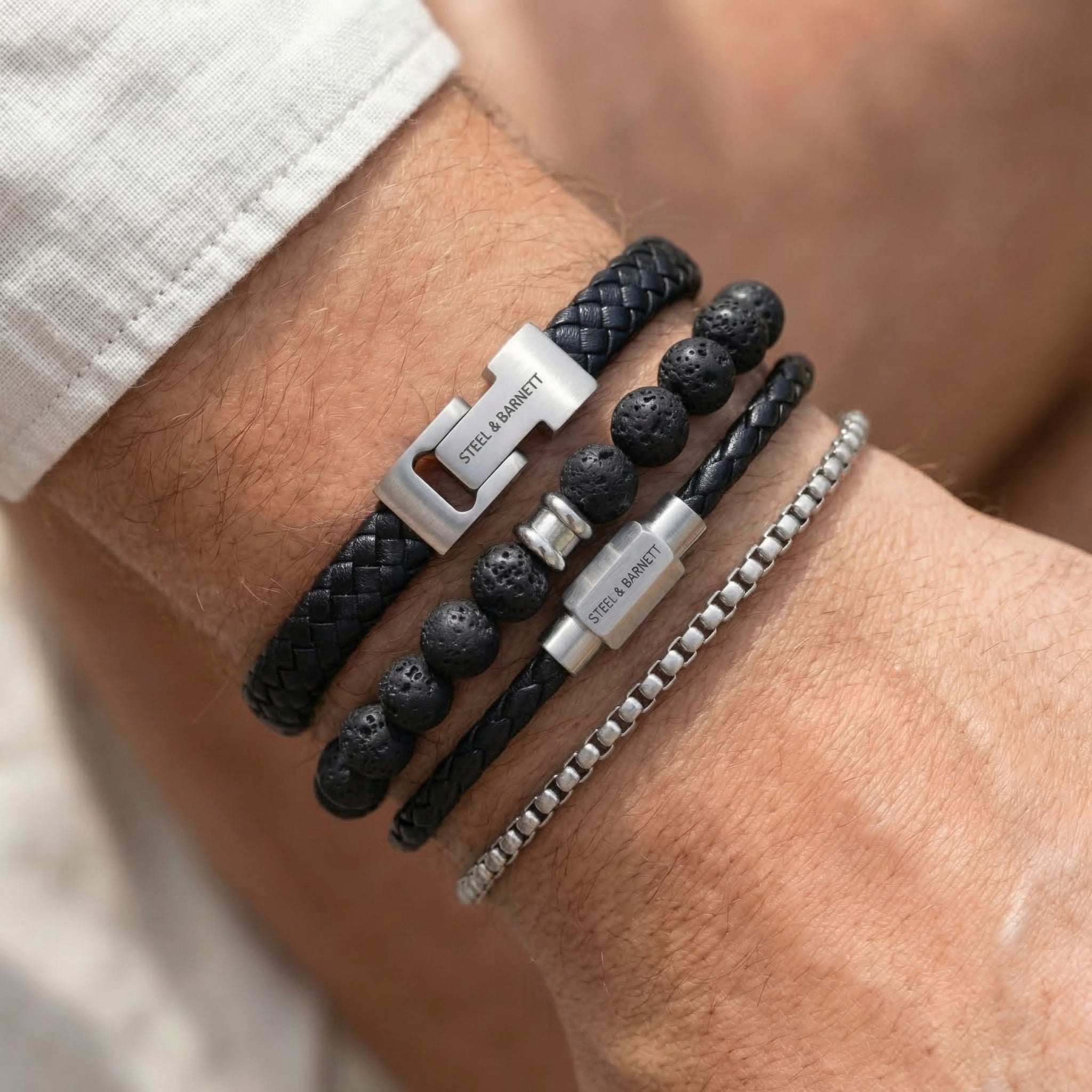 Black braided leather men's bracelet set with lava stone beads and stainless steel clasps in layered look on wrist
