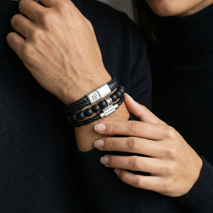Layered black leather men’s bracelet set with matte black beads and brushed stainless steel clasps worn on wrist with dark sweater