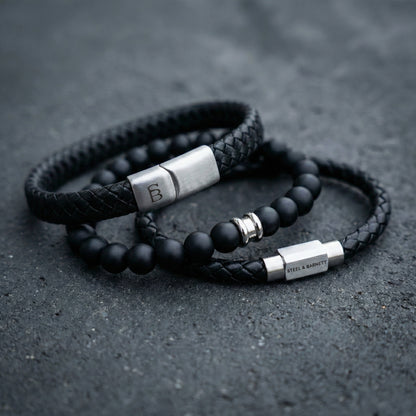 Black braided leather men’s bracelet set with matte black bead bracelet and brushed stainless steel clasp detail on dark stone surface