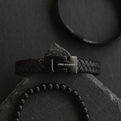 black leather men’s bracelet with braided leather design and black stainless steel clasp shown on a dark stone surface with bead bracelet detail