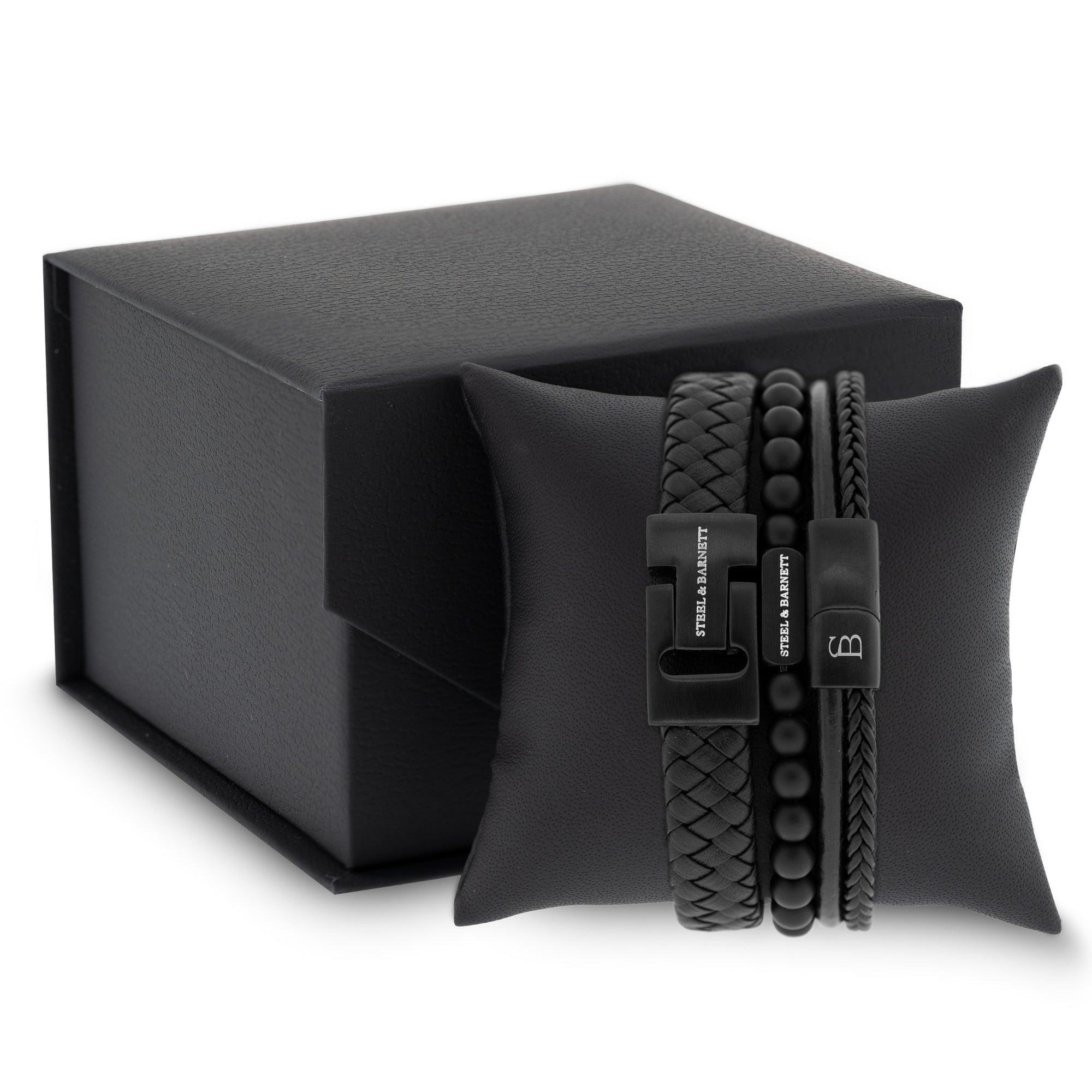 stacked black leather men’s bracelets with braided strands and matte bead design featuring black stainless steel clasps displayed on a cushion beside a gift box