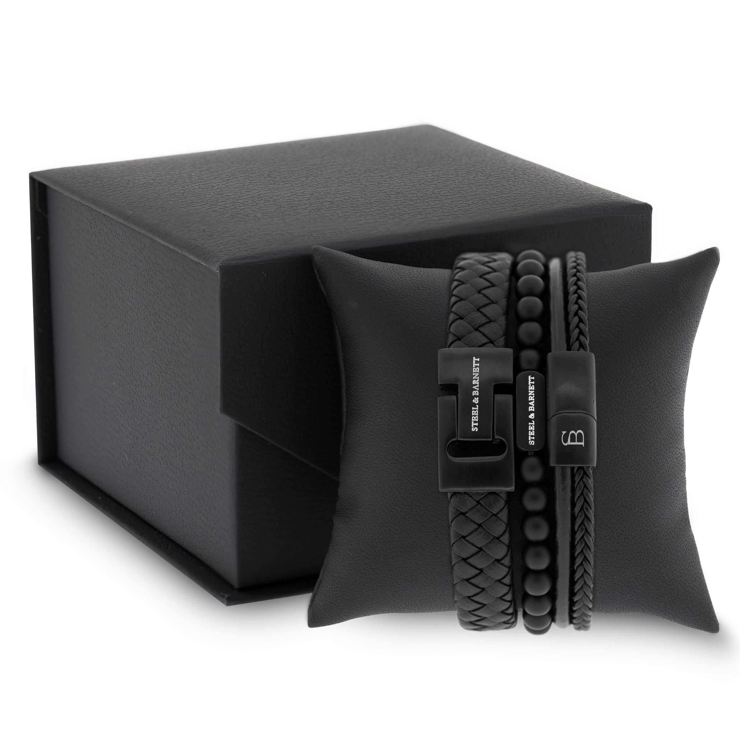 stacked black leather men’s bracelets with braided strands and matte bead design featuring black stainless steel clasps displayed on a cushion beside a gift box