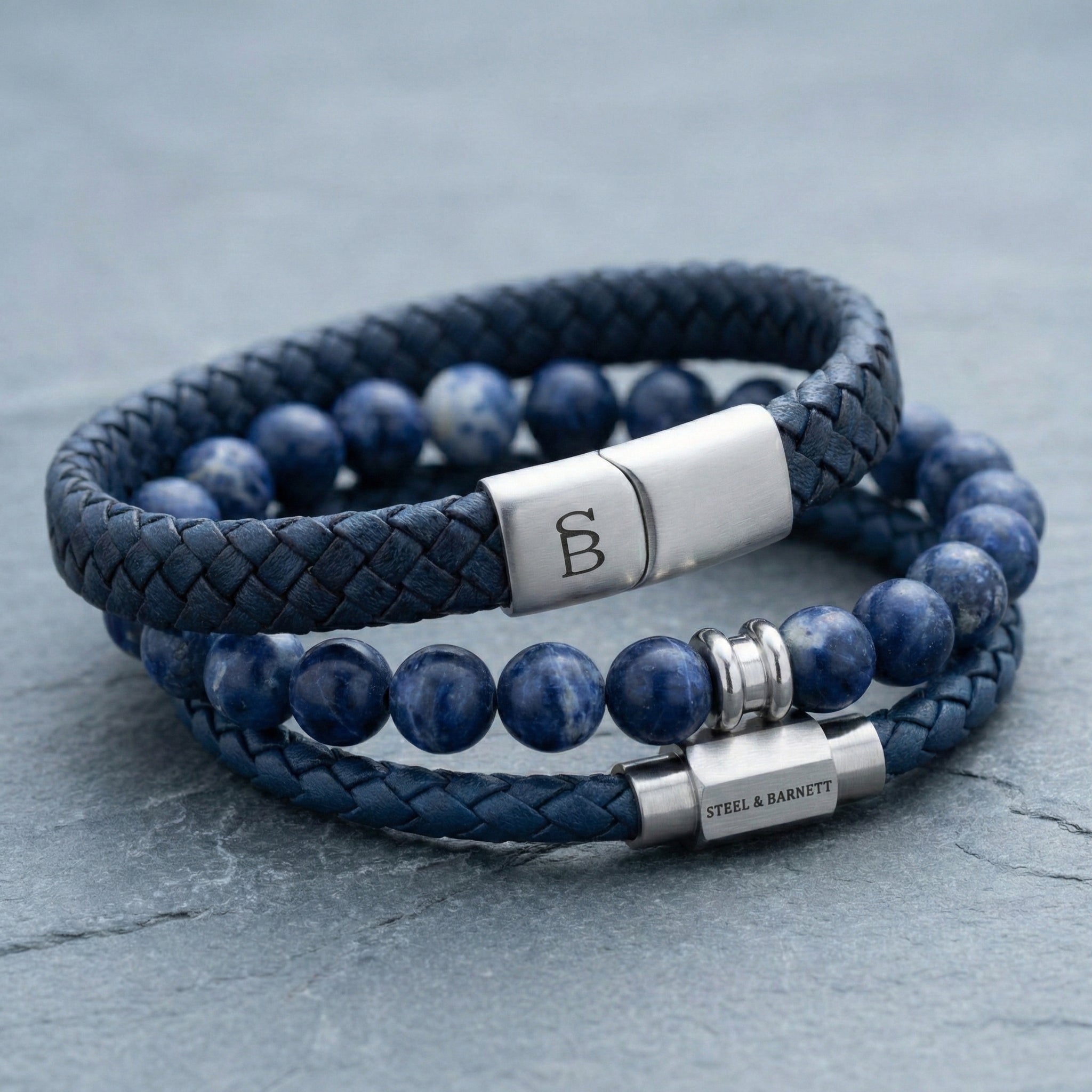 Blue braided leather men’s bracelet with natural stone beads and brushed stainless steel clasp detail on stone surface