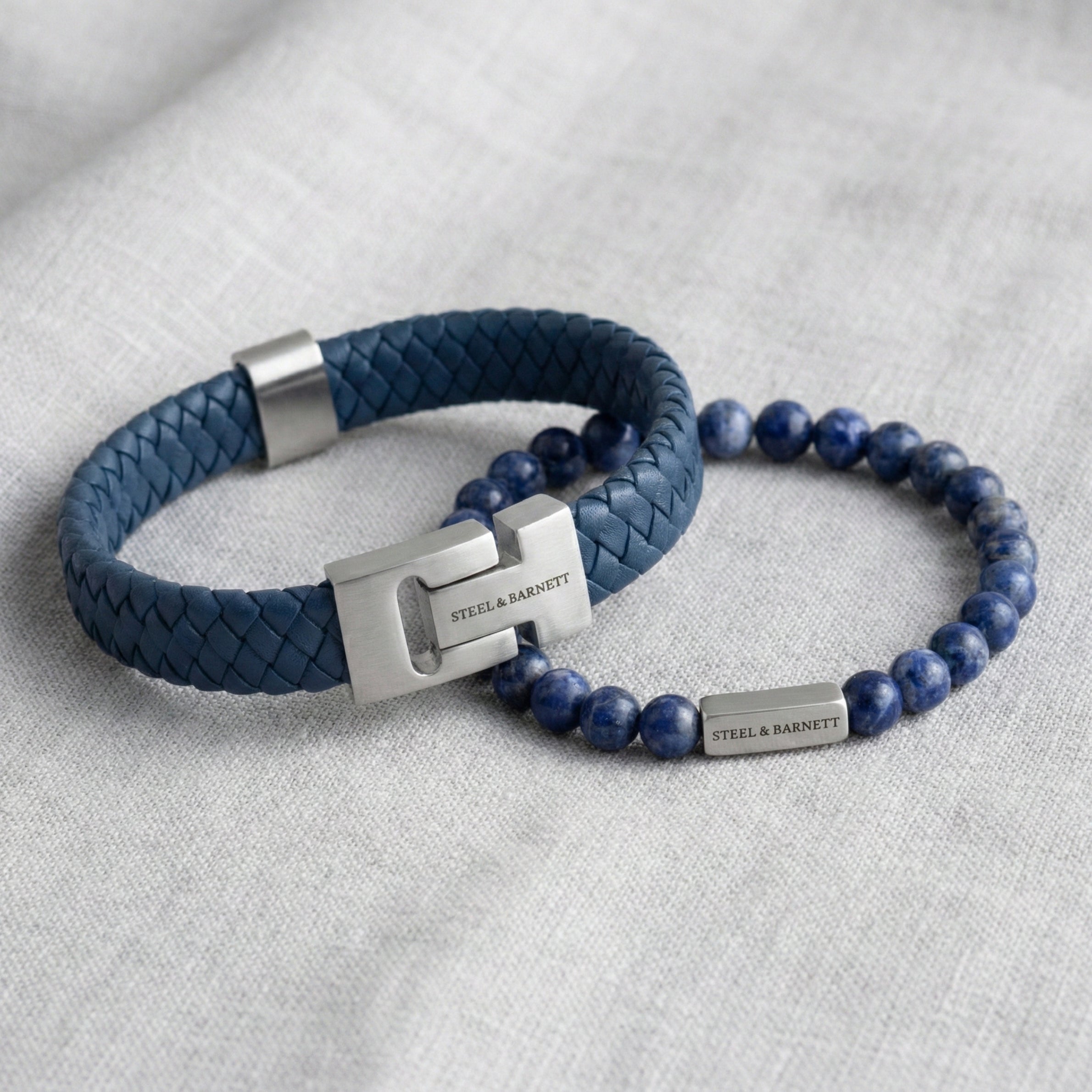 Blue braided leather men’s bracelet with brushed stainless steel clasp and natural stone bead bracelet arranged in a flat lay on light fabric
