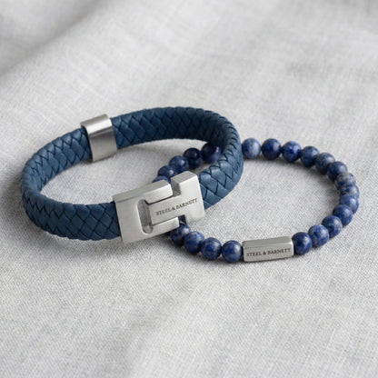 Blue braided leather men’s bracelet with brushed stainless steel clasp and natural stone bead bracelet arranged in a flat lay on light fabric