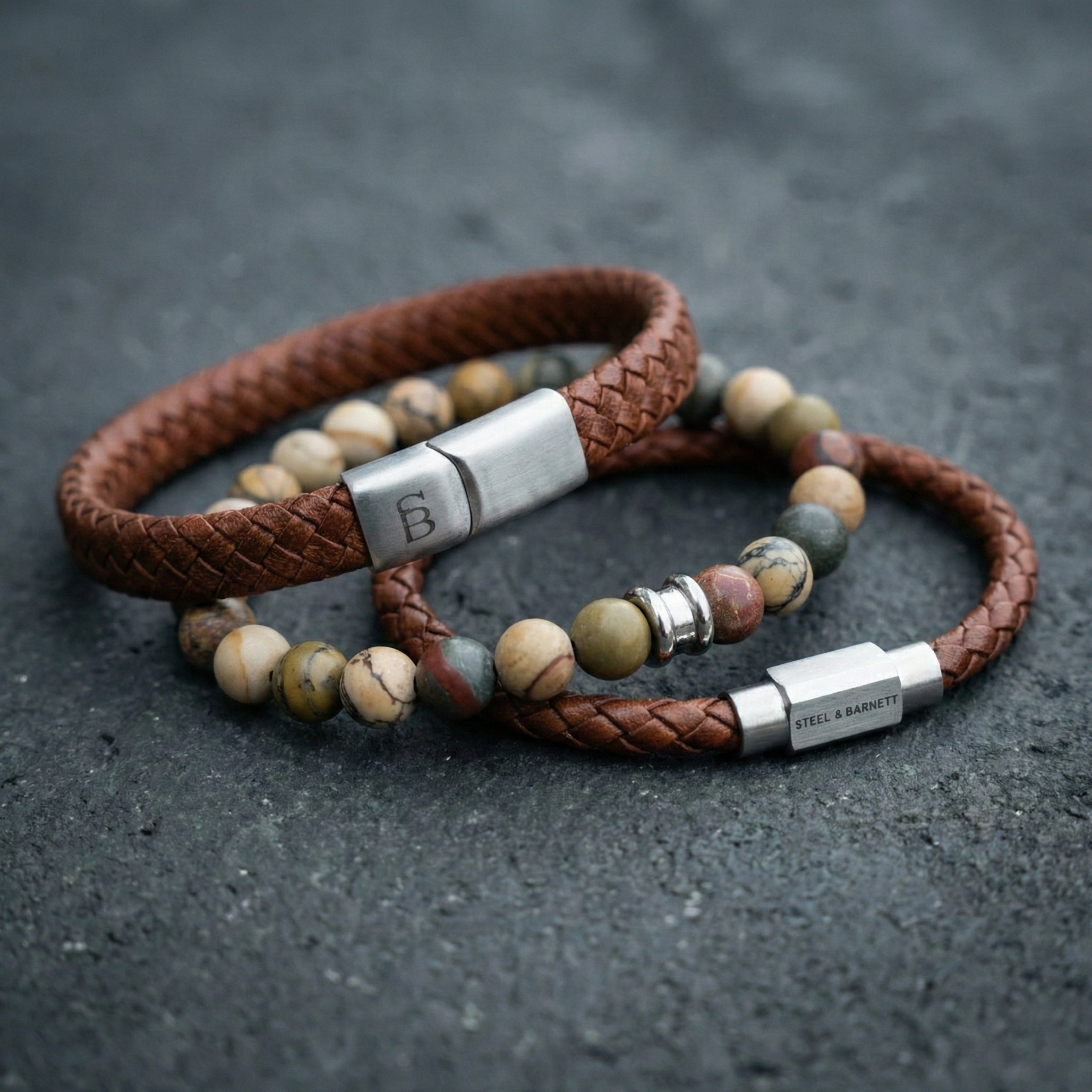 Cognac braided leather men’s bracelet with multicolor natural stone beads and brushed stainless steel clasp detail on dark stone surface