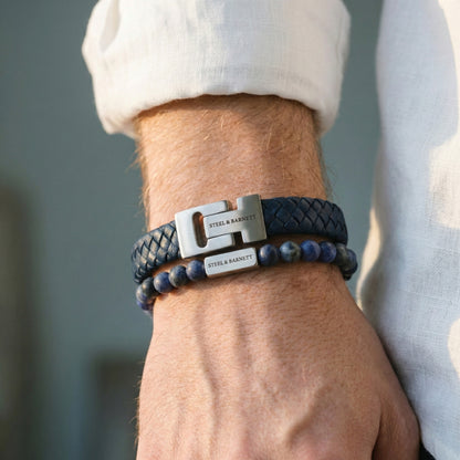Blue braided leather men’s bracelet with brushed stainless steel clasp and beaded design worn on wrist in natural light