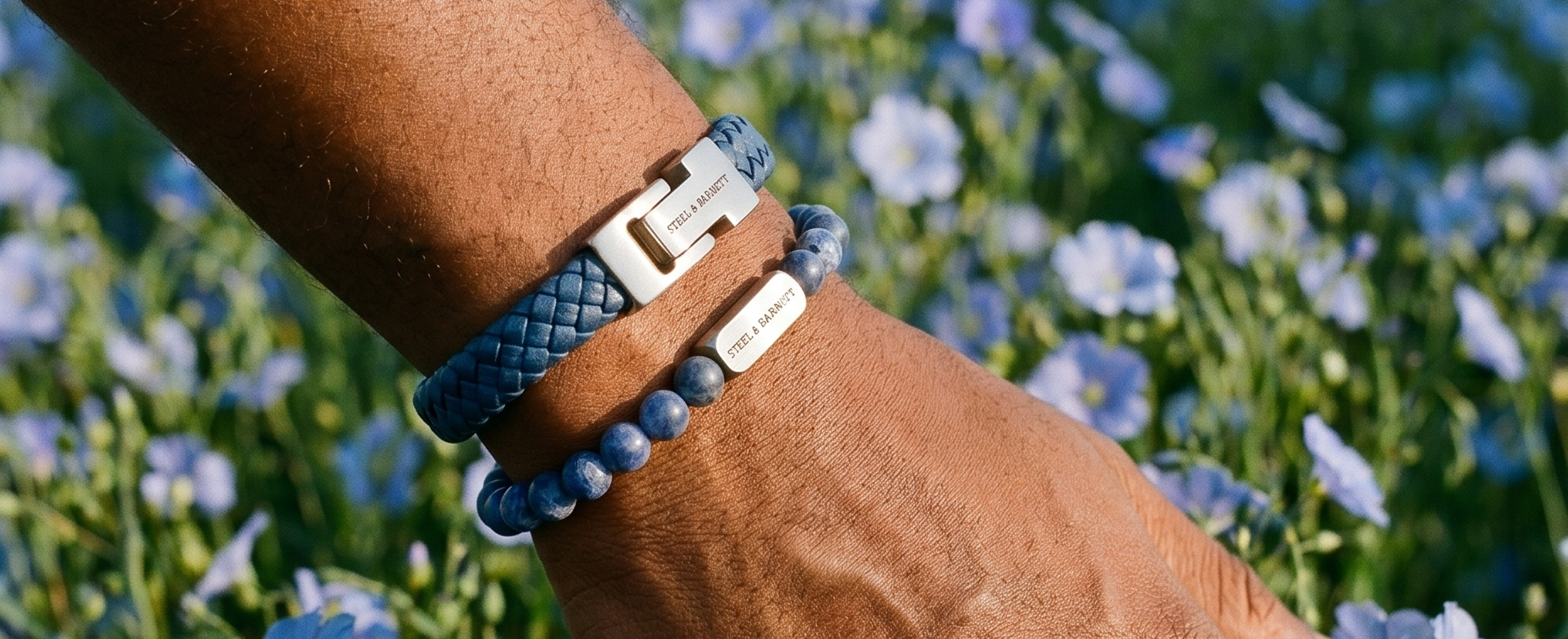 Hand wearing multiple bracelets in a field of blue flowers