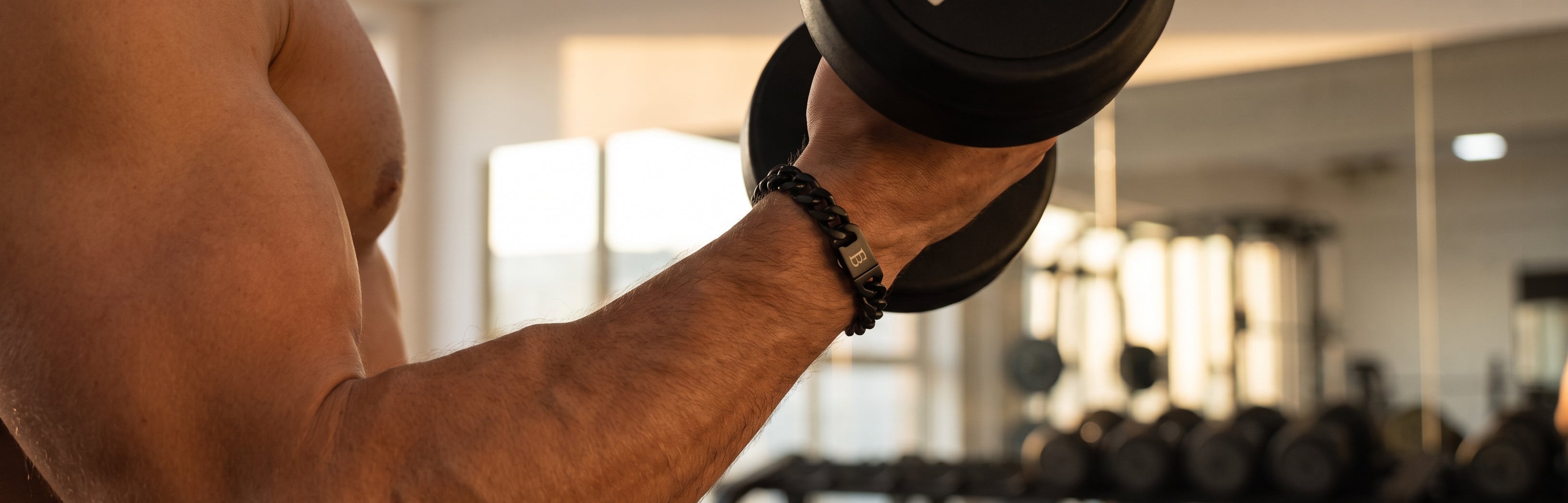 Black chain men's bracelet with a dark metal clasp worn on the wrist while lifting a dumbbell in a gym