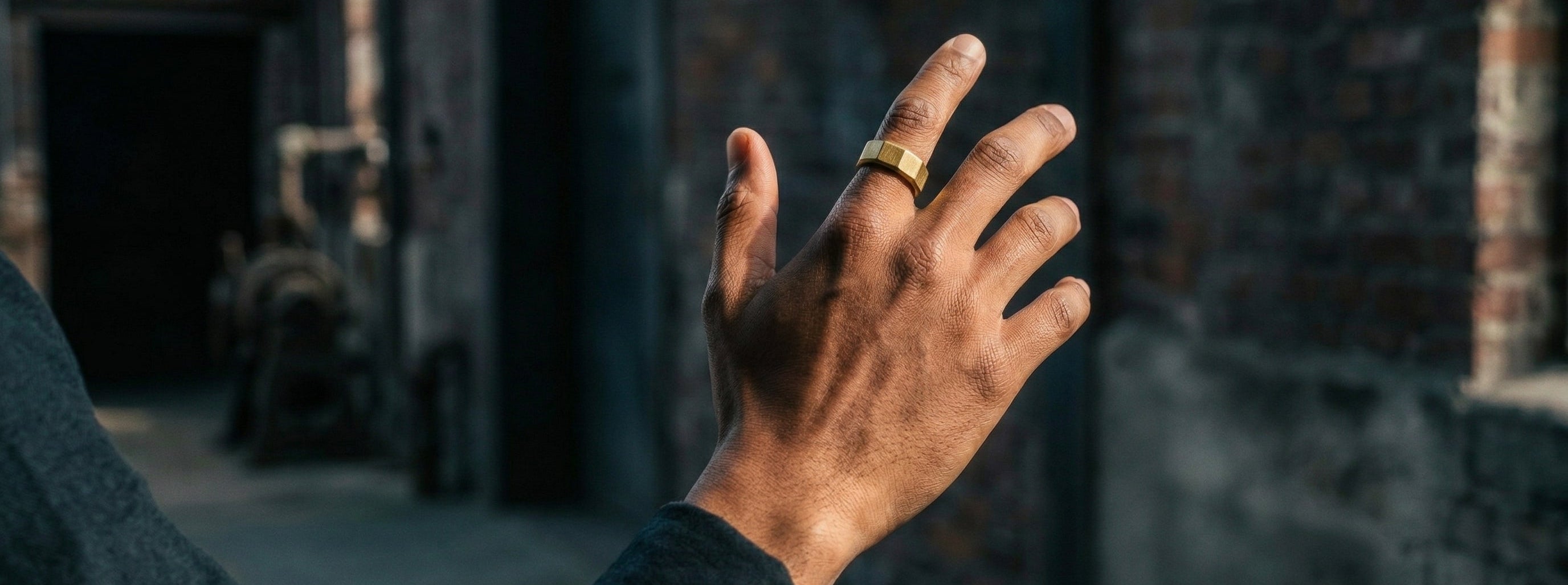 Gold toned men's ring with brushed geometric design worn on finger in an outdoor industrial setting