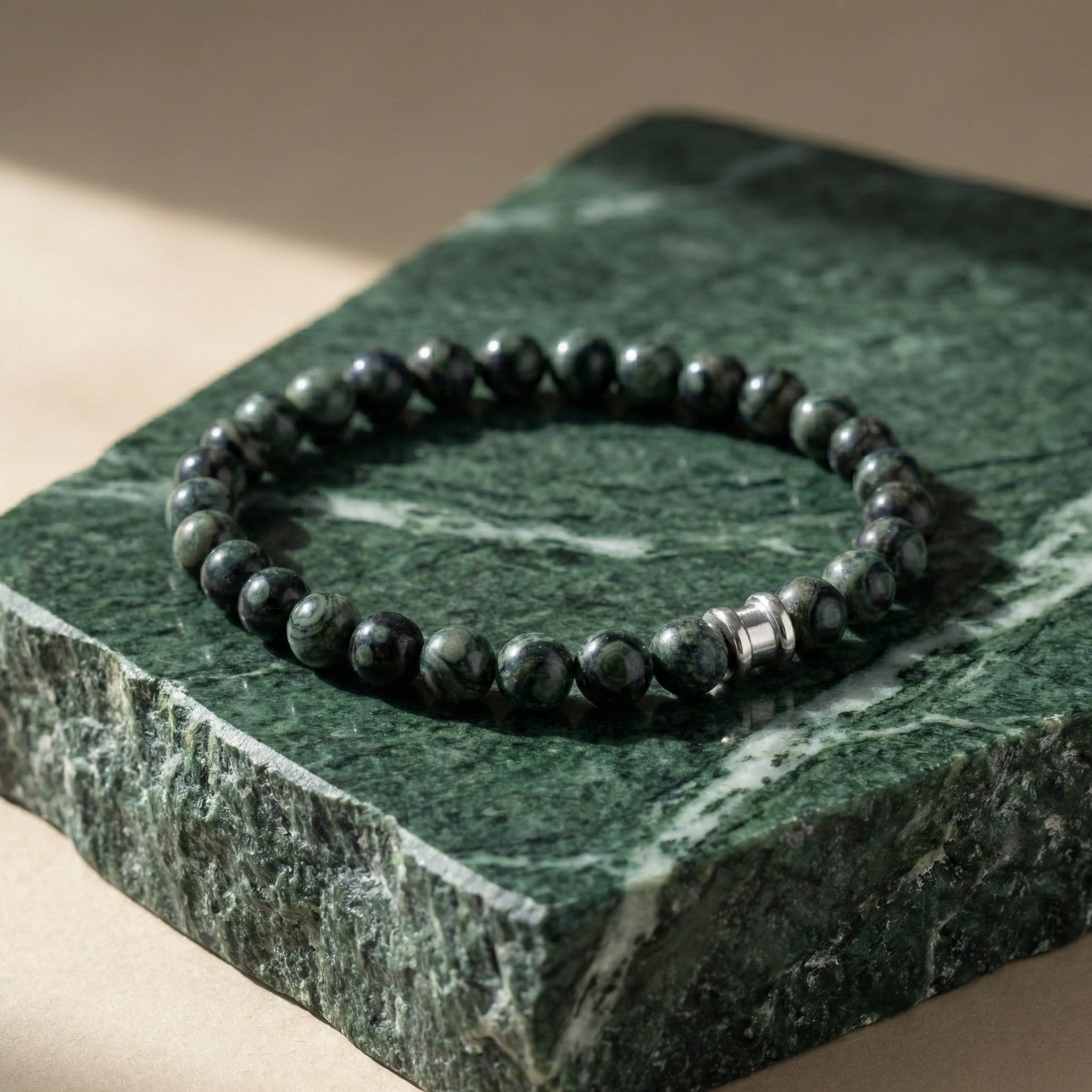 Dark green kambaba stone men's bracelet with polished beads and stainless steel detail on a green marble surface