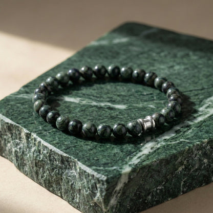 Dark green kambaba stone men's bracelet with polished beads and stainless steel detail on a green marble surface