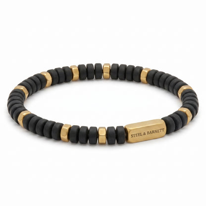 A beaded stretch bracelet featuring matte black round beads alternating with polished gold square spacer beads, with a gold rectangular clasp engraved with the brand name 'STEEL & BARNETT'.