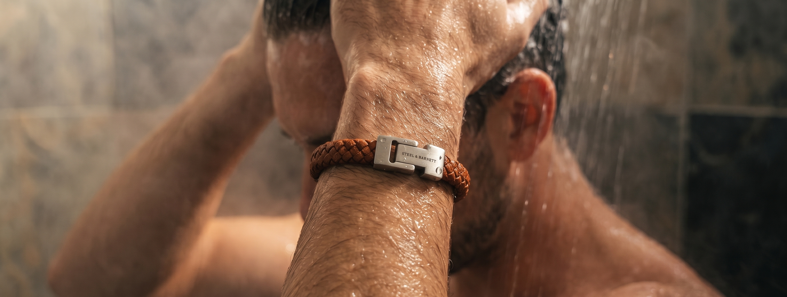 Brown braided leather men’s bracelet with stainless steel clasp worn on wrist under running water in shower setting