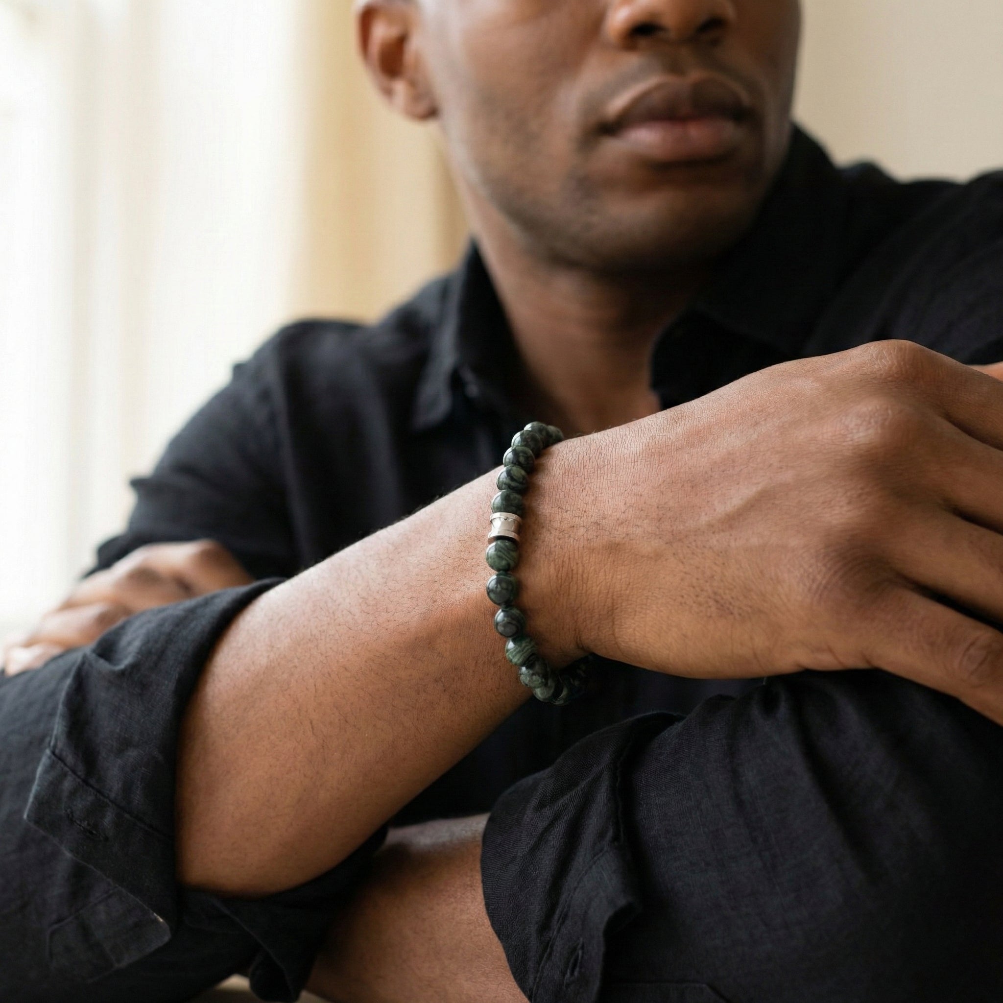 Dark green kambaba stone men's bracelet with round beads and a stainless steel accent worn on wrist