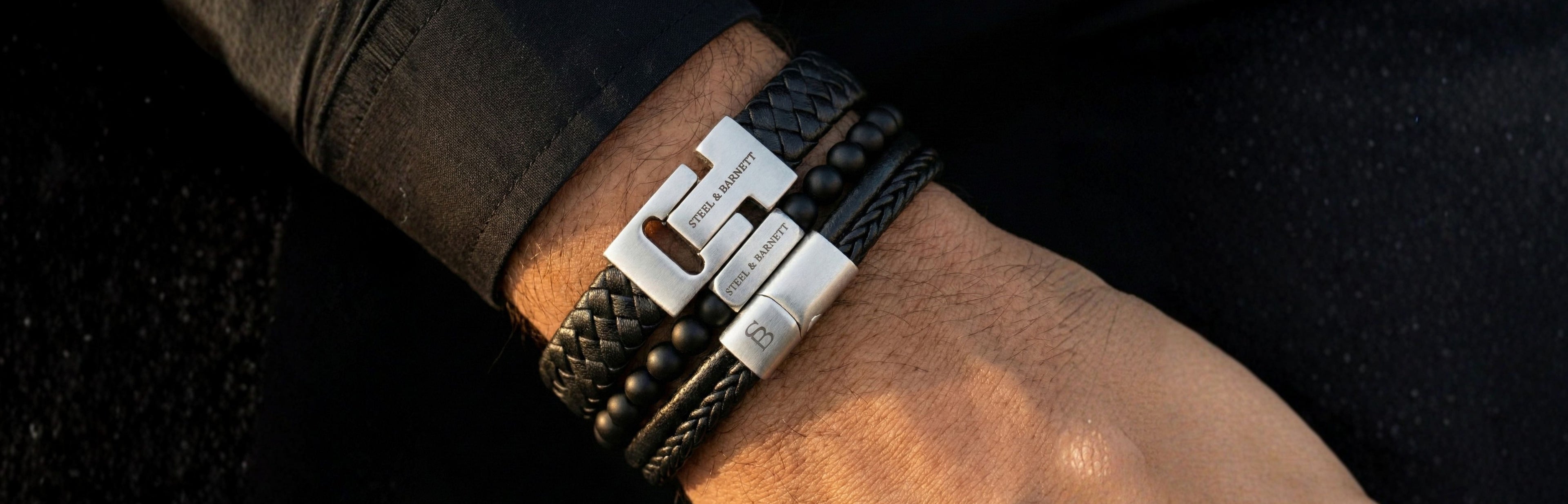 A close-up of a man's wrist wearing a black leather wrap bracelet with a silver-toned metal clasp.