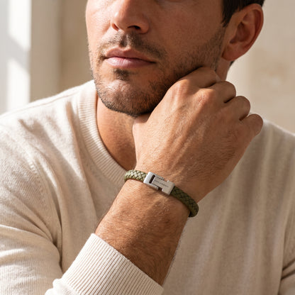 A close-up of a man wearing a green braided bracelet with a silver metal clasp, resting his hand on his chin.
