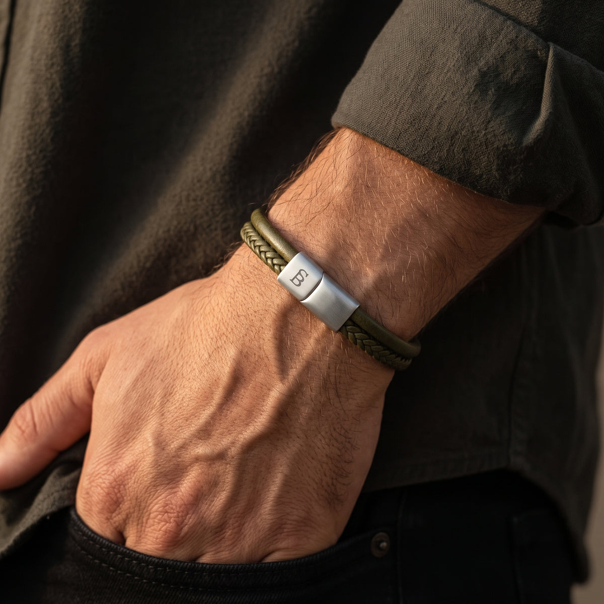 A close-up of a man's wrist wearing a braided olive green bracelet with a silver metal clasp