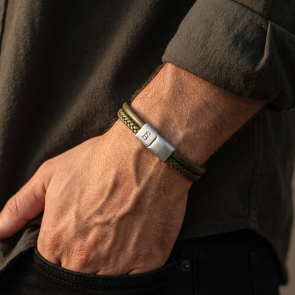 A close-up of a man's wrist wearing a braided olive green bracelet with a silver metal clasp