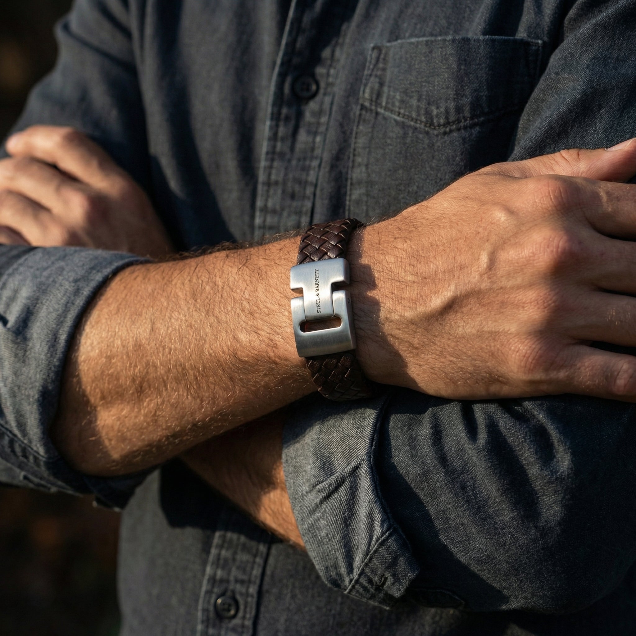 Brown braided leather men’s bracelet with brushed stainless steel clasp worn on wrist with a dark shirt