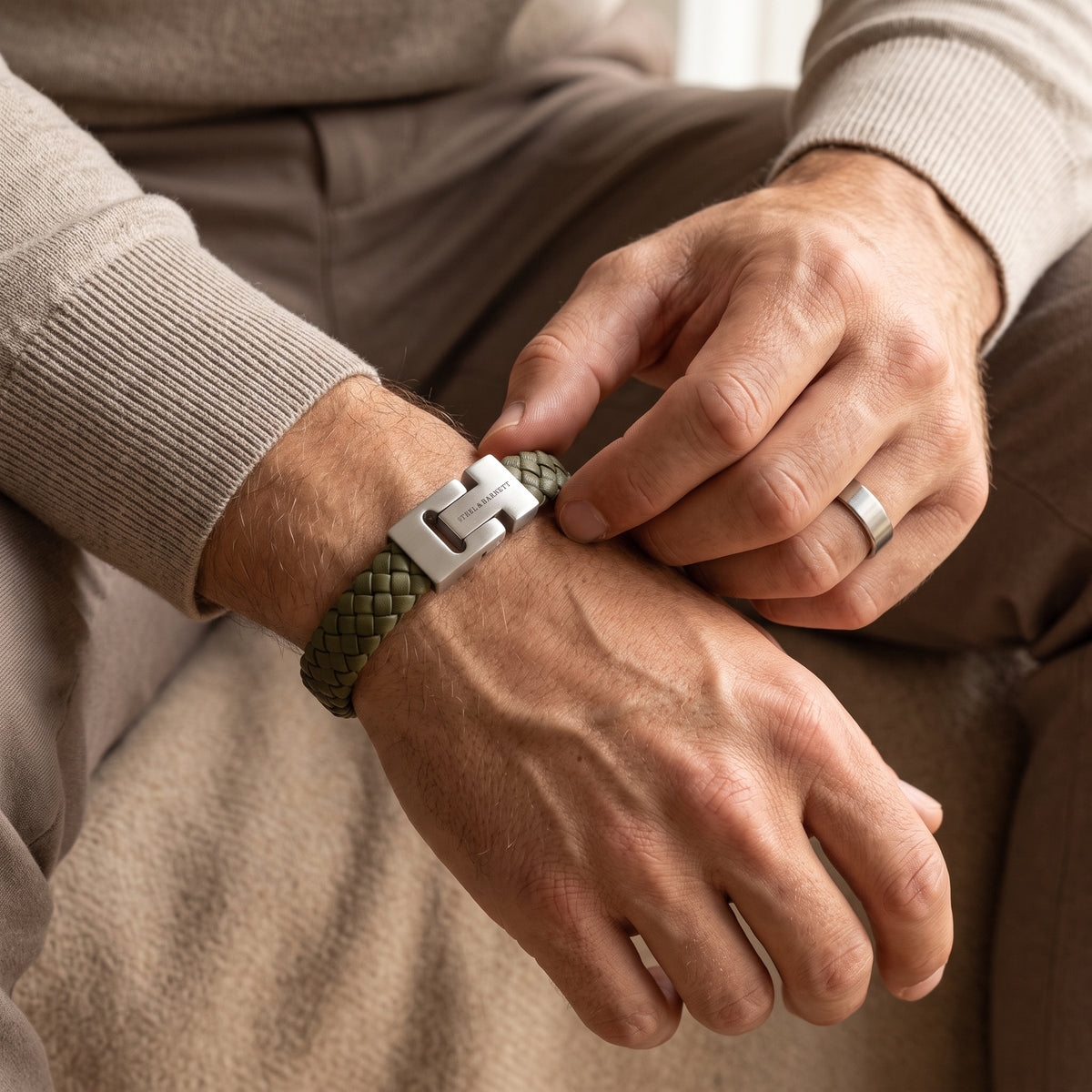 Olive green braided leather men's bracelet with a brushed stainless steel clasp being adjusted on a wrist